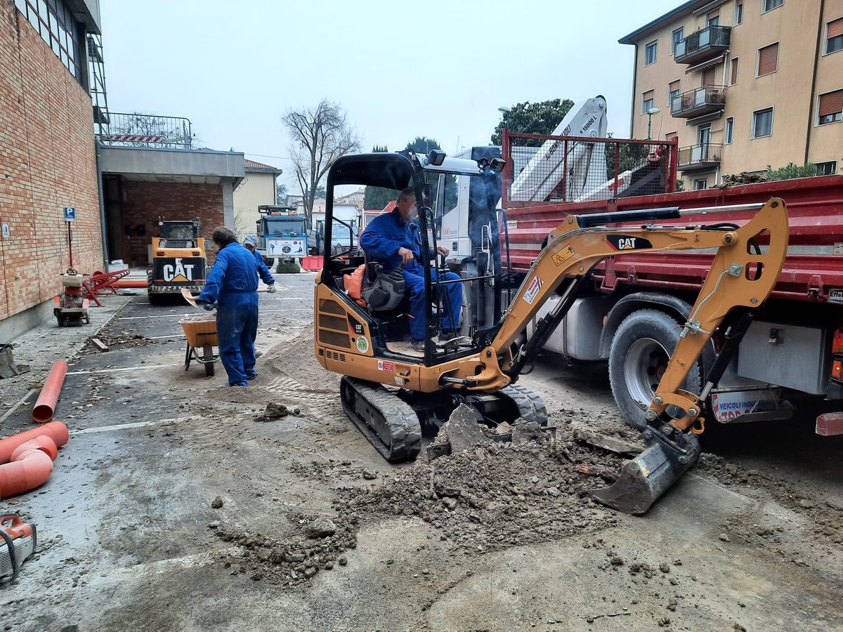 Mini-escavatore della MI.RO. Servizi al lavoro in un cortile condominiale, con due operatori